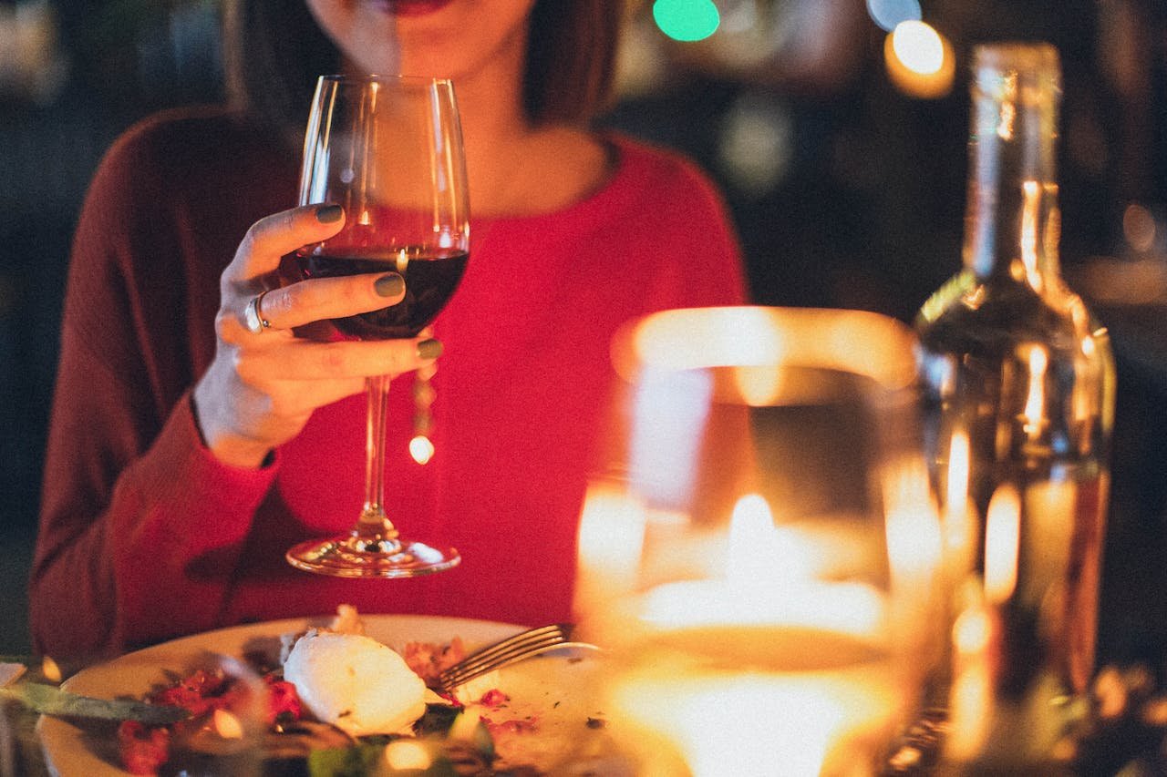 A woman enjoying red wine at a romantic candlelit dinner, perfect for celebrations.